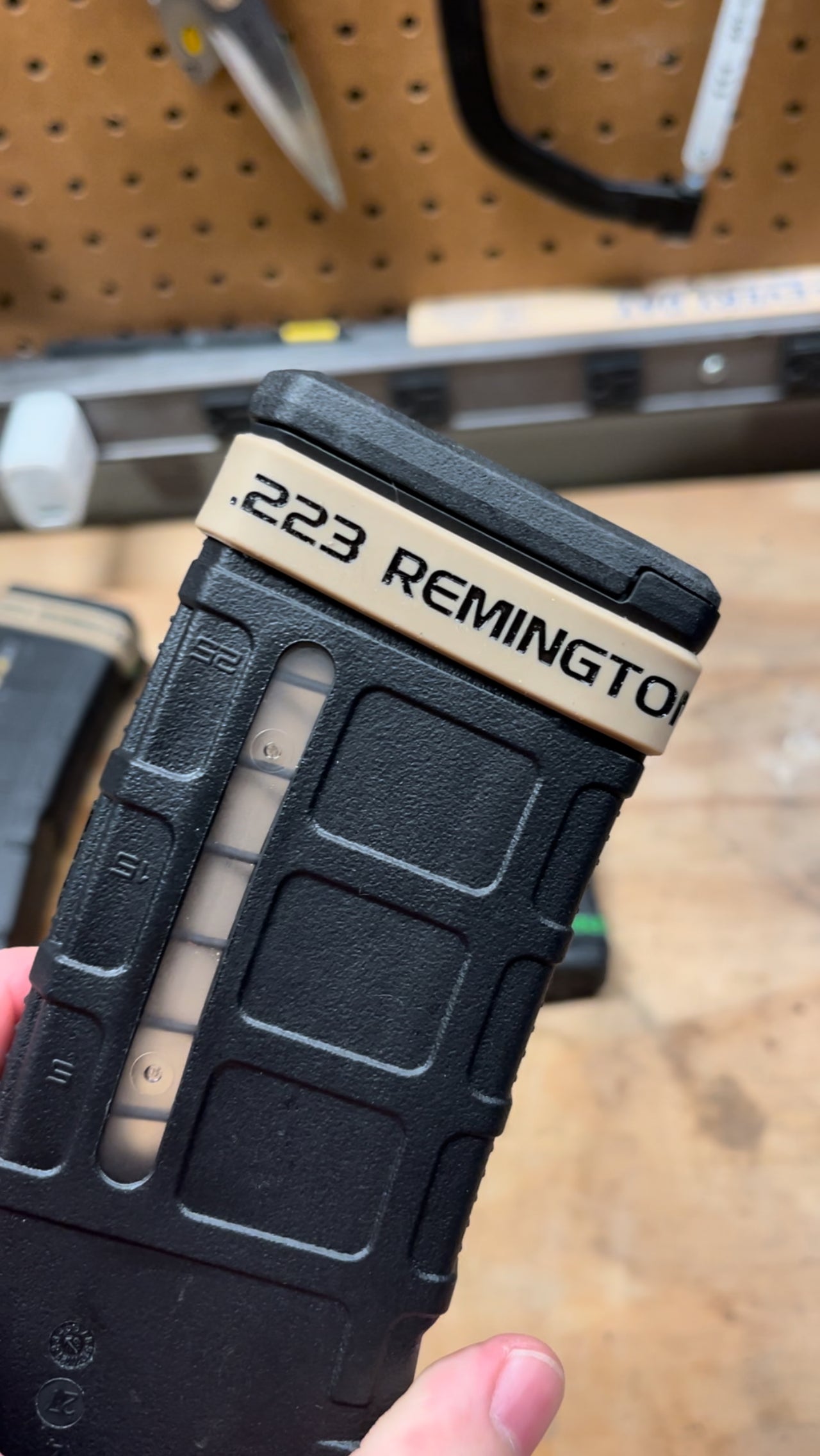 Black rifle magazine with '223 Remington' text held by a hand against a blurred background